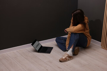 Cyber bullying. Upset teenage girl and laptop with text You Loser on floor indoors. Space for text