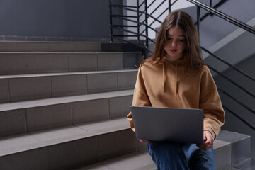Cyber bullying. Upset teenage girl with laptop on stairs indoors. Space for text