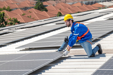 A solar panel installer wearing a hard hat and safety gear is installing solar panels on a roof.