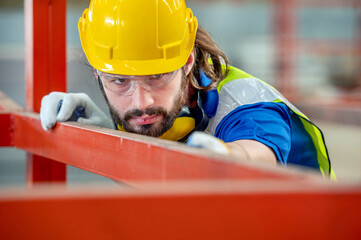 A man wearing a hard hat and safety glasses inspects a metal beam at a construction site