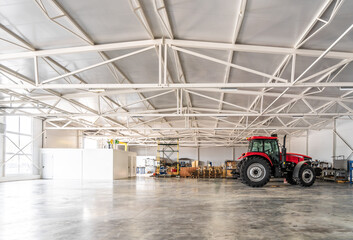 Tractor inside modern industrial warehouse with high metal ceiling. Agriculture technology, warehouse logistics, farm equipment and industrial innovation concept.