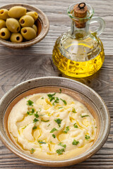Turnip Skordalia. Creamy Greek dip made of turnips, garlic, and olive oil. A bottle of olive oil and a bowl with green olives behind.