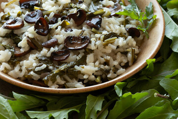 A plate of arugula risotto with champignons among fresh arugula leaves. Close-up.