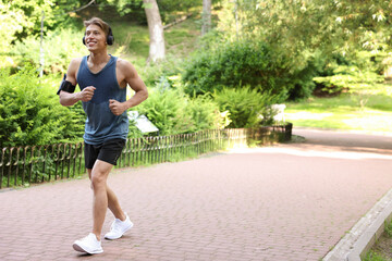 Sporty man with headphones running in park, space for text