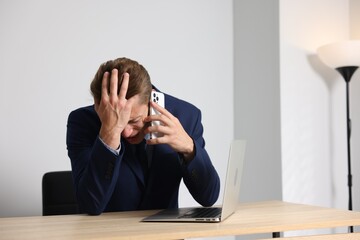 Young businessman with laptop complaining to someone via phone at wooden table indoors, space for...