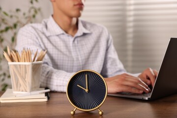 Deadline. Alarm clock and man working on laptop at wooden table, selective focus