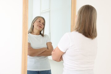 Beautiful senior woman looking at herself in mirror indoors