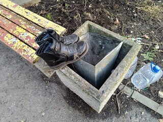 Discarded old boots on a park bench next to a trash bin in a minimalistic style