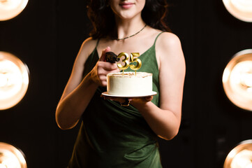 Woman in green dress holds a birthday cake with number 35 candles, while aiming a gun.