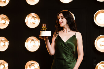 Woman in green dress holds a birthday cake with number 35 candles. Celebratory mood, glamorous...