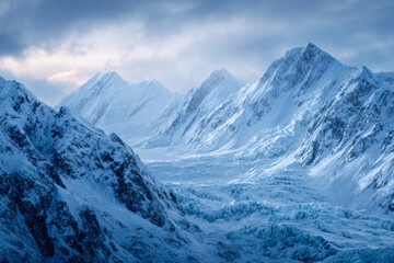 Obraz premium Majestic snow covered mountains and glacial valley under a dramatic cloudy sky