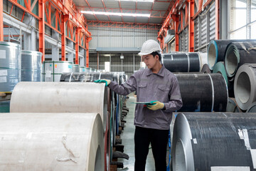 A worker dressed in hardhat and  protective glove, stand in a factory check material while holding...