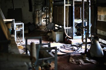 Rusted pipes and scattered cables in a deteriorating industrial workshop with broken machinery