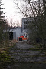 Rusty, orange forklift on overgrown yard in front of desolate industrial building