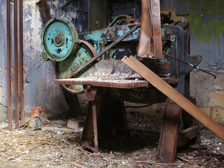 Rusted industrial machine in abandoned workshop surrounded by debris and peeling paint