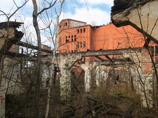 Abandoned factory complex with red brick structure framed by crumbling walls and bare trees