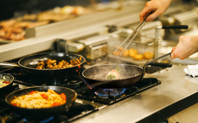 Close-up of chef’s hands cooking multiple dishes on gas stove in a busy restaurant kitchen. Steaming food, sizzling pans, and authentic culinary process.