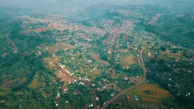 rone view over Kapchorwa, Eastern Uganda, shows a vast settlement on Mount Elgon's slopes, with red-soil roads, farmland plots, and green vegetation stretching under hazy sky conditions.