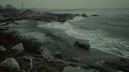 Misty shoreline landscape featuring crashing waves against rock formations and gloomy skies,