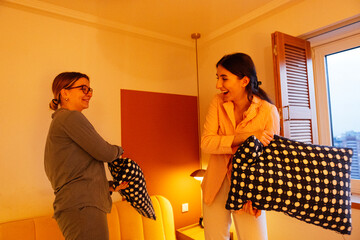 Two young girls are fighting with pillows in the bedroom. Carefree friends in pajamas laugh and...