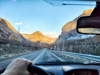 Driving through a scenic mountain road during golden hour with warm sunlight illuminating the...