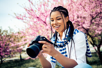 Young woman with braided hair enjoying photography on a spring day amidst blooming flowers and a...