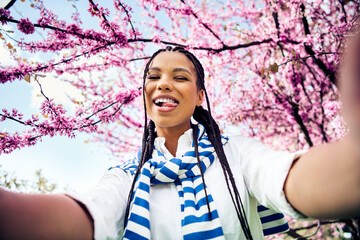 Charming woman captures cheerful selfie outdoors surrounded by blooming spring blossoms during a...