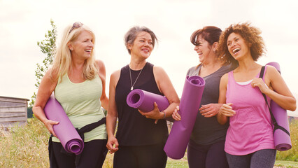 Group Of Mature Female Friends On Outdoor Yoga Retreat Walking Along Path Through Campsite