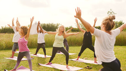 Female Teacher Leading Group Of Mature Men And Women In Class At Outdoor Yoga Retreat