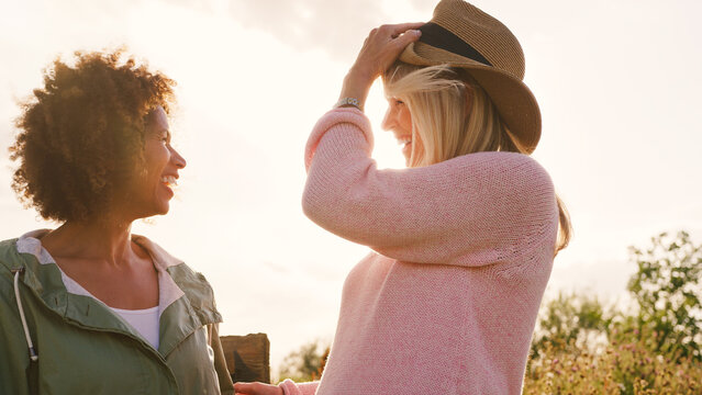 Outdoor Portrait Of Two Smiling Mature Female Friends Against Flaring Sun - Powered by Adobe