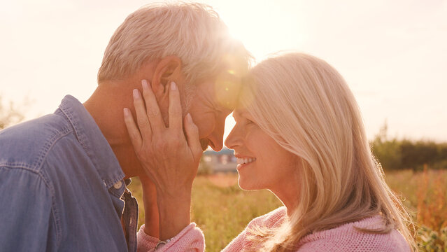 Close Up Of Loving Mature Couple In Countryside Hugging Head To Head Against Flaring Sun