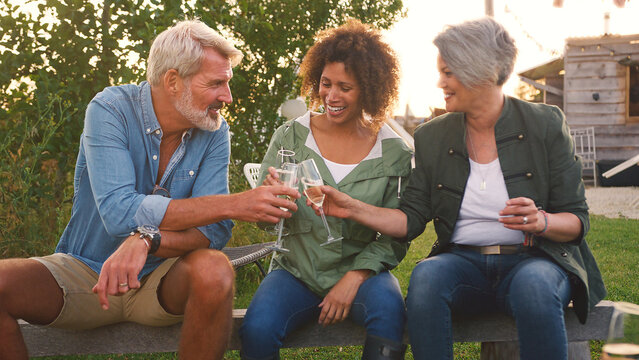 Group Of Mature Friends Sitting Around Fire And Making A Toast At Outdoor Campsite Bar