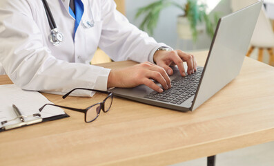 Closeup of professional male medical doctor in white uniform working at the desk in office typing...
