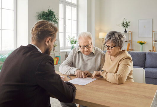 Senior couple sitting at table and having consultation with financial agent about health insurance in retirement. Elderly man and woman studying terms of contract during visit of financial advisor.