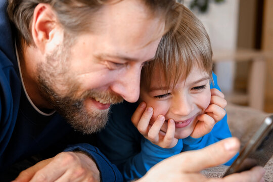 Father and son little boy laughing and using phone. They watching funny videos together, playing games on smartphone. Concept technology, smart phone addicted. Fun weekend activity. Modern fatherhood - Powered by Adobe
