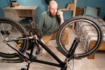 Bearded man talking on phone with mechanic while repairing damaged bike, phone call with bicycle...