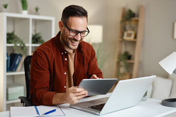 Happy entrepreneur working from home using laptop and tablet smiling