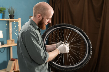 Portrait of bearded man holding bike wheel in hands repairing bicycle at home