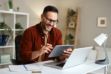Smiling freelancer working from home using laptop and tablet
