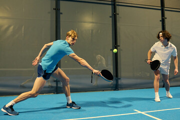 Dynamic young men excel at padel on a vibrant indoor court during a spirited match
