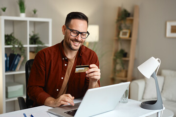Smiling man using laptop and credit card for online shopping at home office