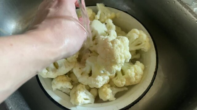 washing fresh cauliflower under kitchen tap water