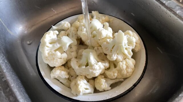 washing fresh cauliflower under kitchen tap water