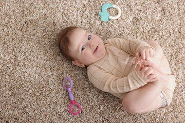 Cute little baby with rattle toy on floor at home, above view. Space for text