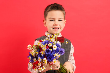 Portrait of smiling little boy with bouquet of beautiful flowers on red background