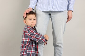Little boy afraid to leave without mother and hugging her on grey background. Separation anxiety