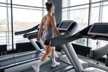 A fit woman confidently walking on a treadmill in a bright and inviting gym, promoting fitness and...