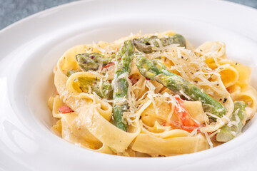 Tagliatelle pasta with creamy garlic sauce, asparagus, peppers, and parmesan topping