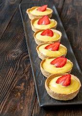 Mini mango cream tarts topped with strawberries lined on elegant black plate