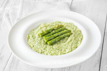 Asparagus risotto served in white plate with whole spears on top